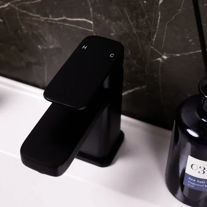 Modern black basin mixer tap on white countertop with dark marble tiles, luxury bathroom decor