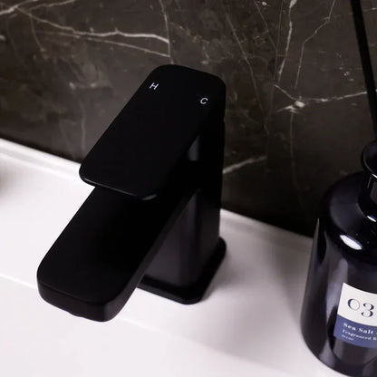 Modern black basin mixer tap on white countertop with dark marble tiles, luxury bathroom decor