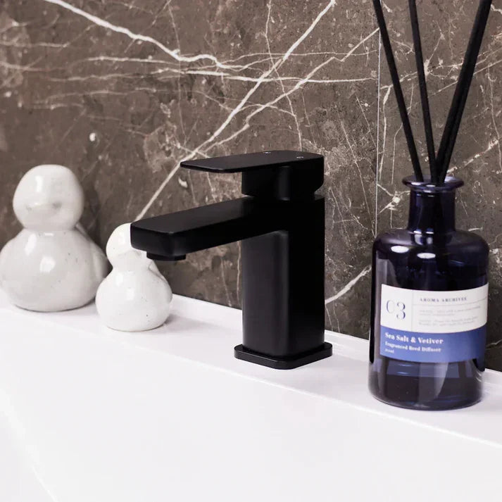 Matte black basin mixer tap on white sink with marble tile backsplash, luxury bathroom decor