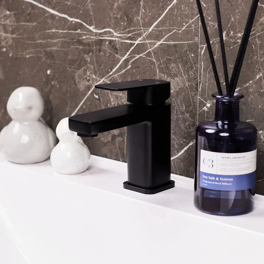 Matte black basin mixer tap on white sink with marble tile backsplash, luxury bathroom decor