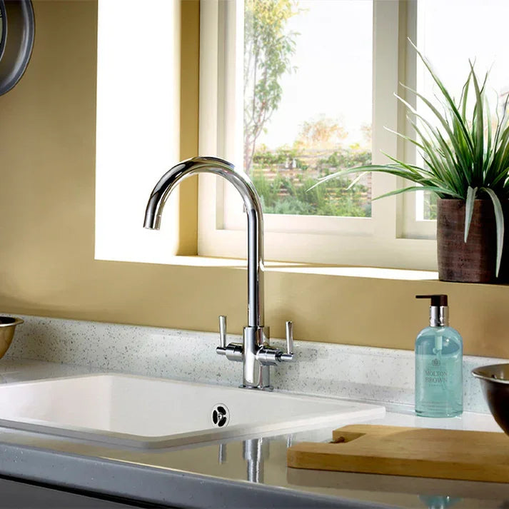 Chrome kitchen mixer tap over white sink with soap dispenser and plant on counter