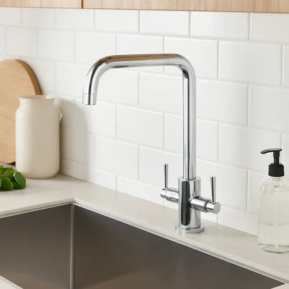 Modern chrome kitchen sink mixer tap with dual handles, set against white subway tiles